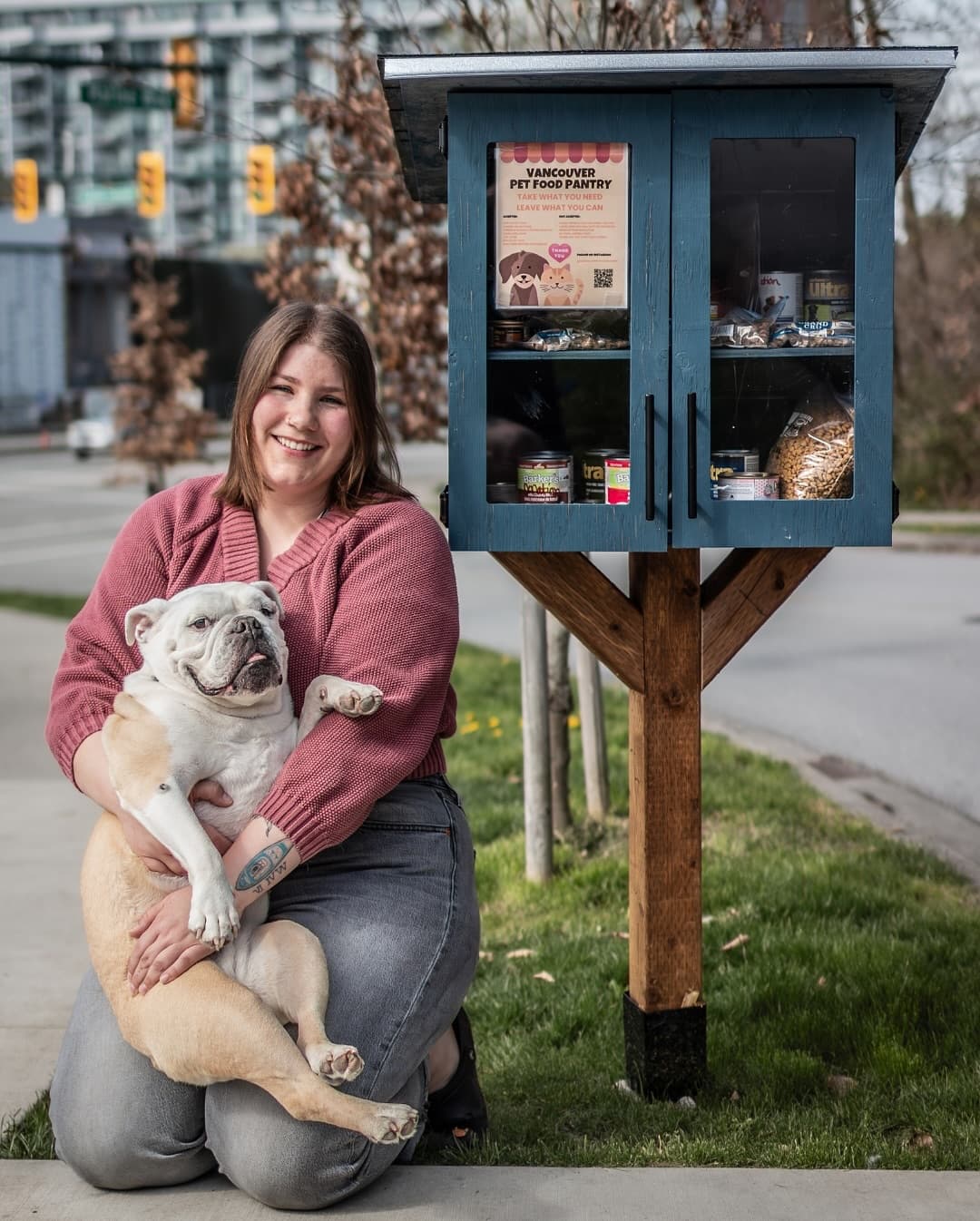 Smiling woman holding a bulldog next to a blue wooden pet food pantry cabinet.